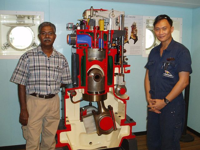 Pastor Moses (left) standing beside a diesel engine of a ship