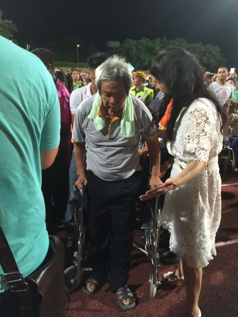 Pastor Callie Liew praying for God to heal a man who came in a wheelchair